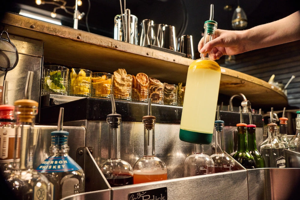 Bartender pulling a Crew Bottle from a well of pre-batched cocktails behind the bar.