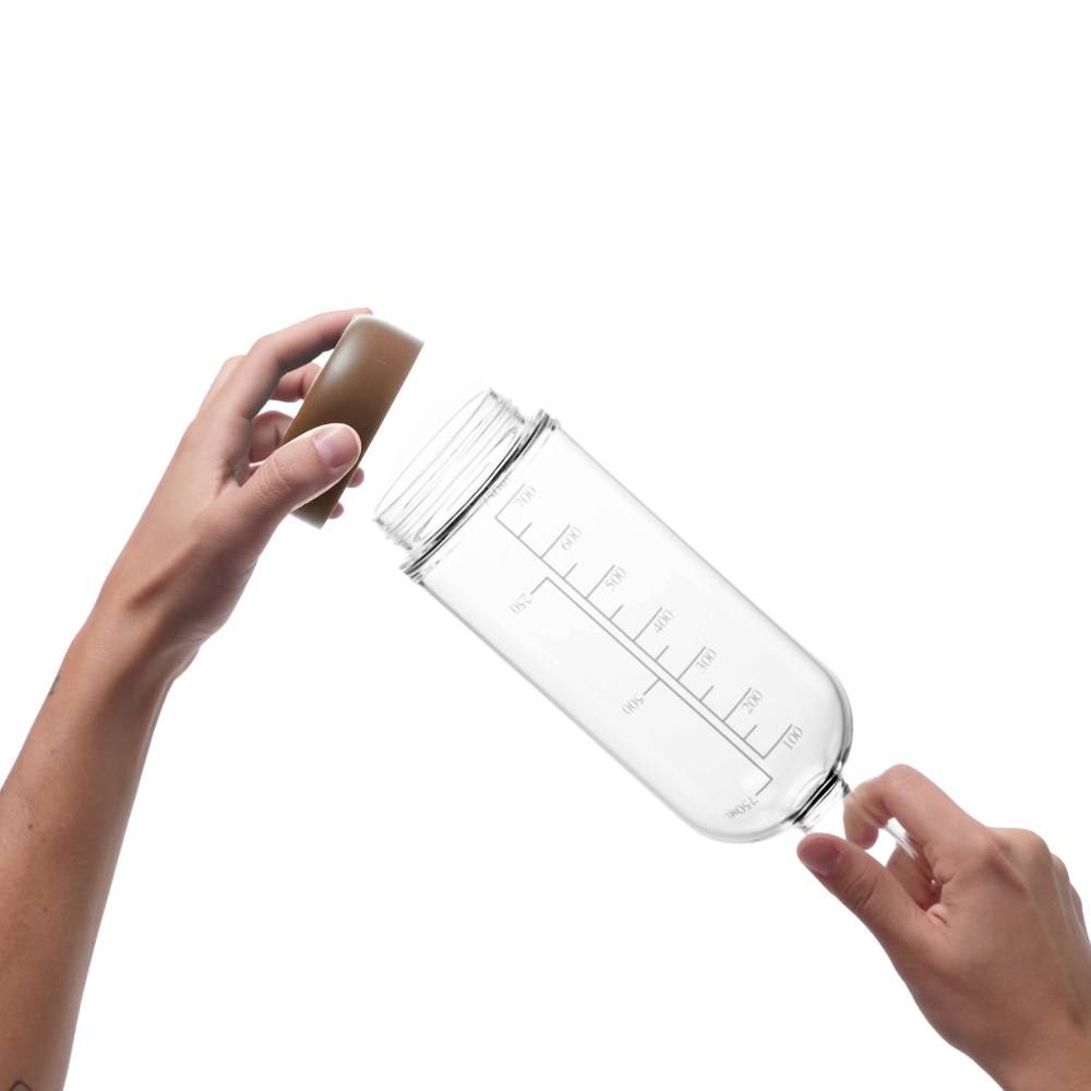 Glass pre-batch bottle with Mocha removable base being held by a person on a white background