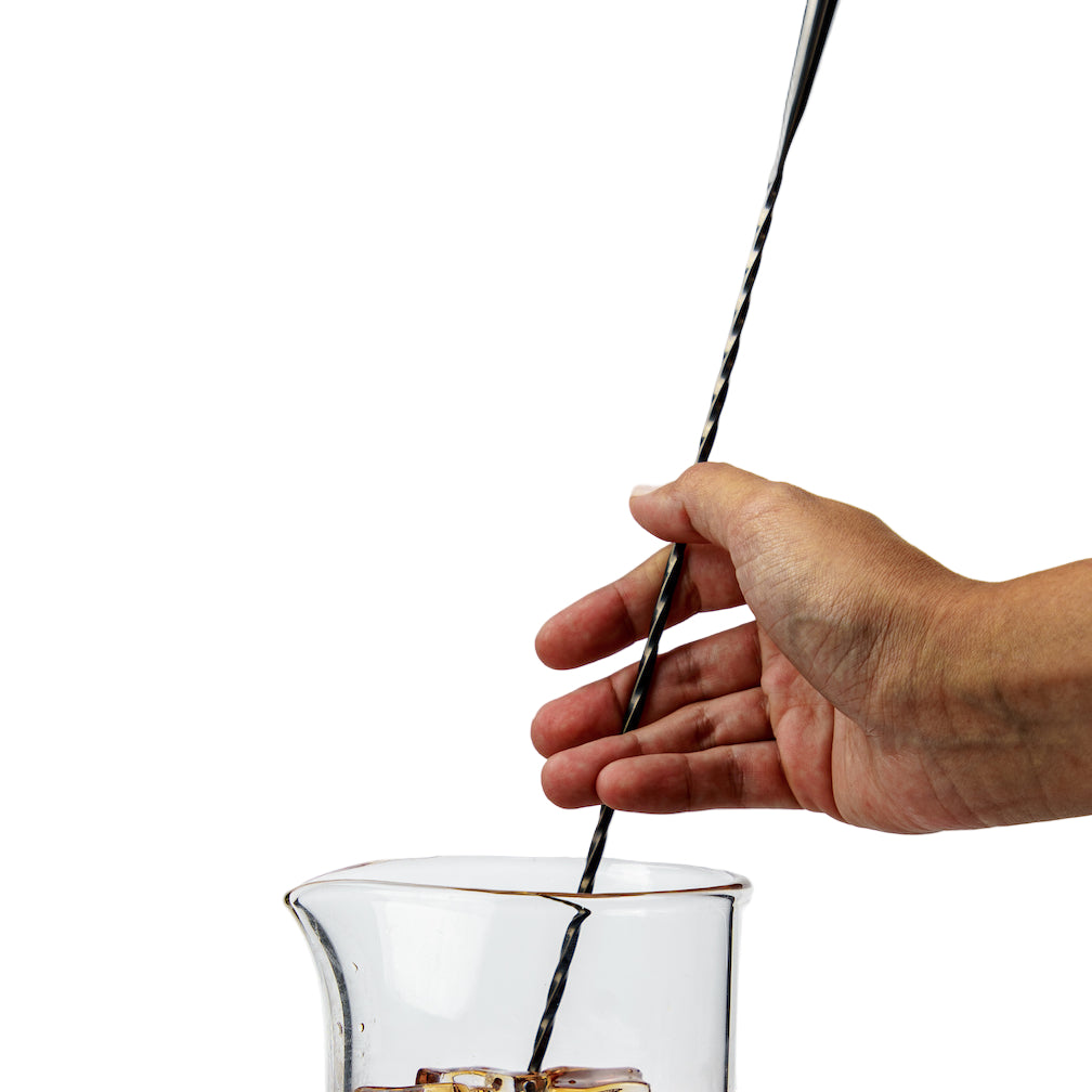 Bartender stirring a bar spoon in a mixing glass with ice and liquid