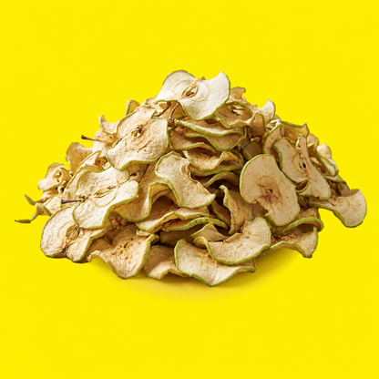 A pile of Garny dried apple slices cocktail garnish with visible seeds, showing light beige and off-white tones with pale green edges, set against a solid bright yellow background.