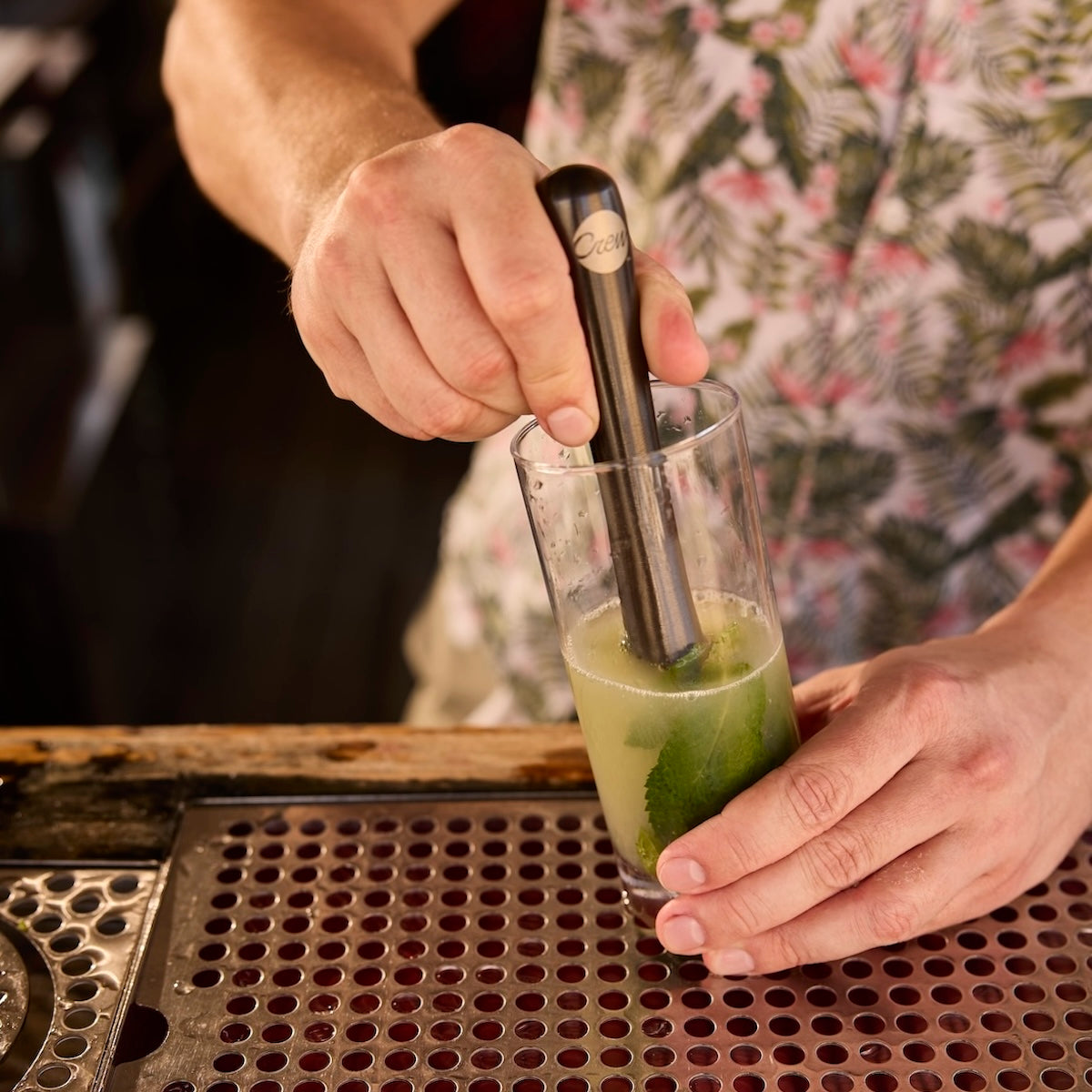 Bartender muddling ingredients in a glass to make a craft cocktail