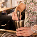 Craft bartender muddling ingredients in a Boston-style cocktail shaker tin with sleek matte black finish