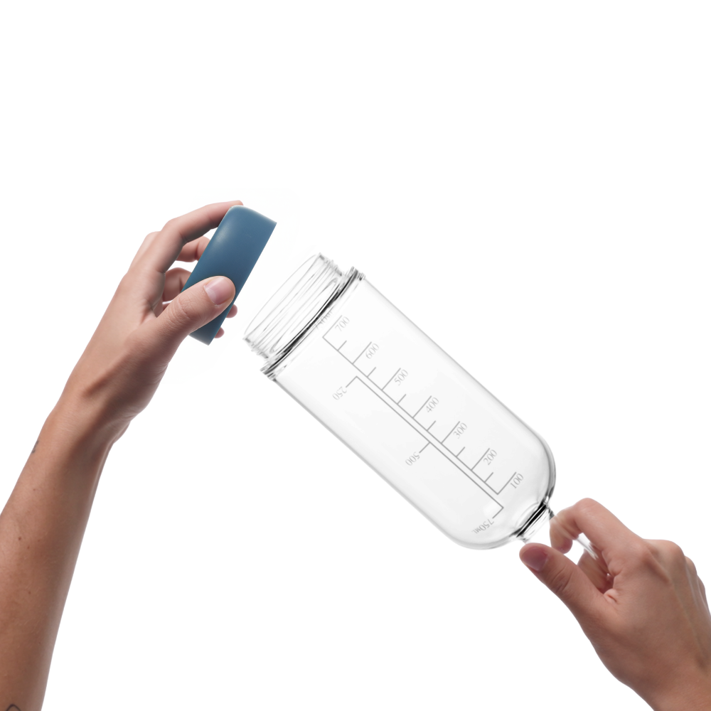 Glass pre-batch bottle with Crew Blue removable base being held by a person on a white background